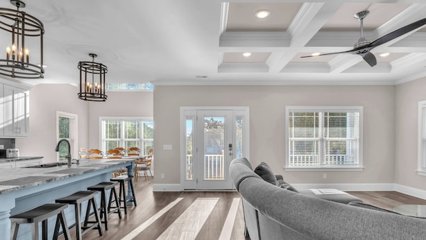 A modern kitchen with a bar area, wooden flooring, and a gray sofa in the living area.