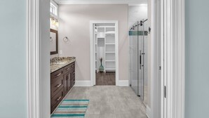 A narrow hallway with a bathroom on the left, a closet with shelves, and a glass shower on the right.