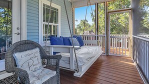 A porch with a swing chair and a bench, both with blue cushions.