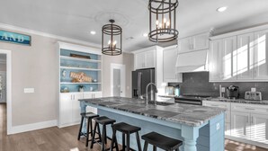 A modern kitchen with a central island, bar stools, white cabinets, and pendant lighting.