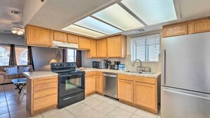 Cocina compacta con armarios de madera, refrigerador de acero inoxidable, lavavajillas y estufa negra.