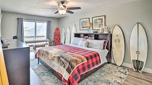 Un dormitorio con cama, escritorio, ventilador de techo y tablas de surf apoyadas en la pared.