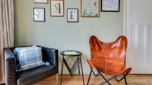 Una habitación con un sofá de cuero negro, un sillón de cuero marrón, una mesita redonda y una puerta blanca.