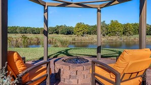 Ein Pavillon mit Feuerstelle und zwei orangenen Sesseln, mit Blick auf einen See und einen gepflegten Rasen.
