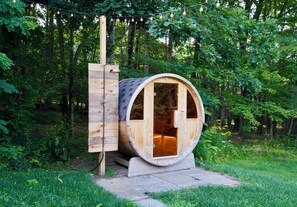 A wooden barrel-shaped structure with a door, a small porch, and a light fixture above.