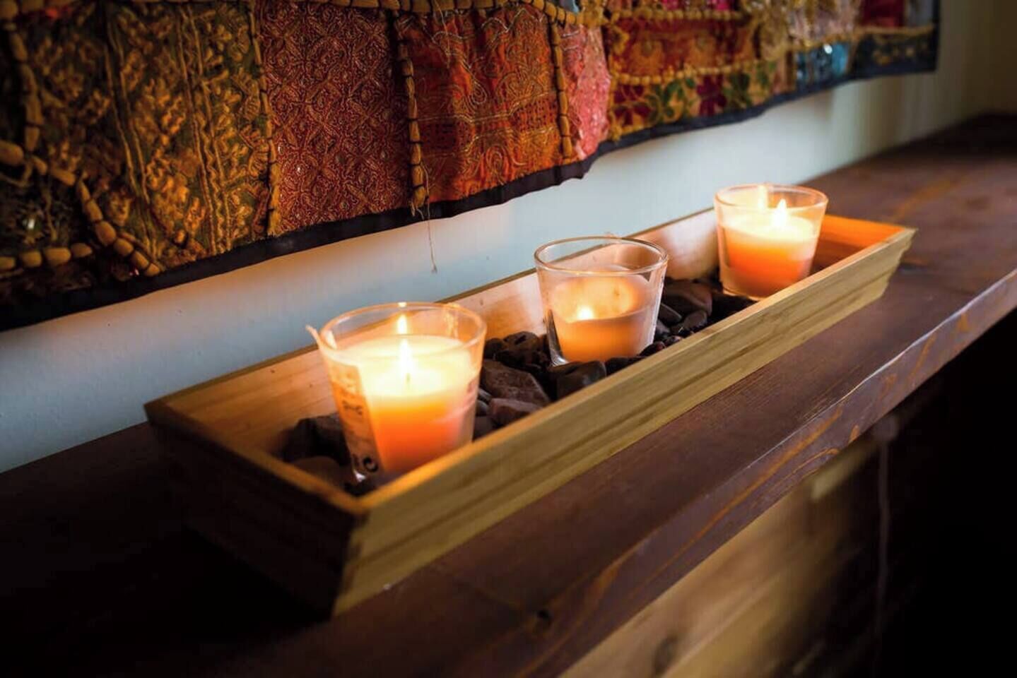 A wooden tray with three lit candles on a wooden surface.