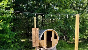 Eine Holzbott-artige Konstruktion mit einer Tür, umgeben von einem Kiesweg, mit Lichterketten in einem bewaldeten Gebiet.