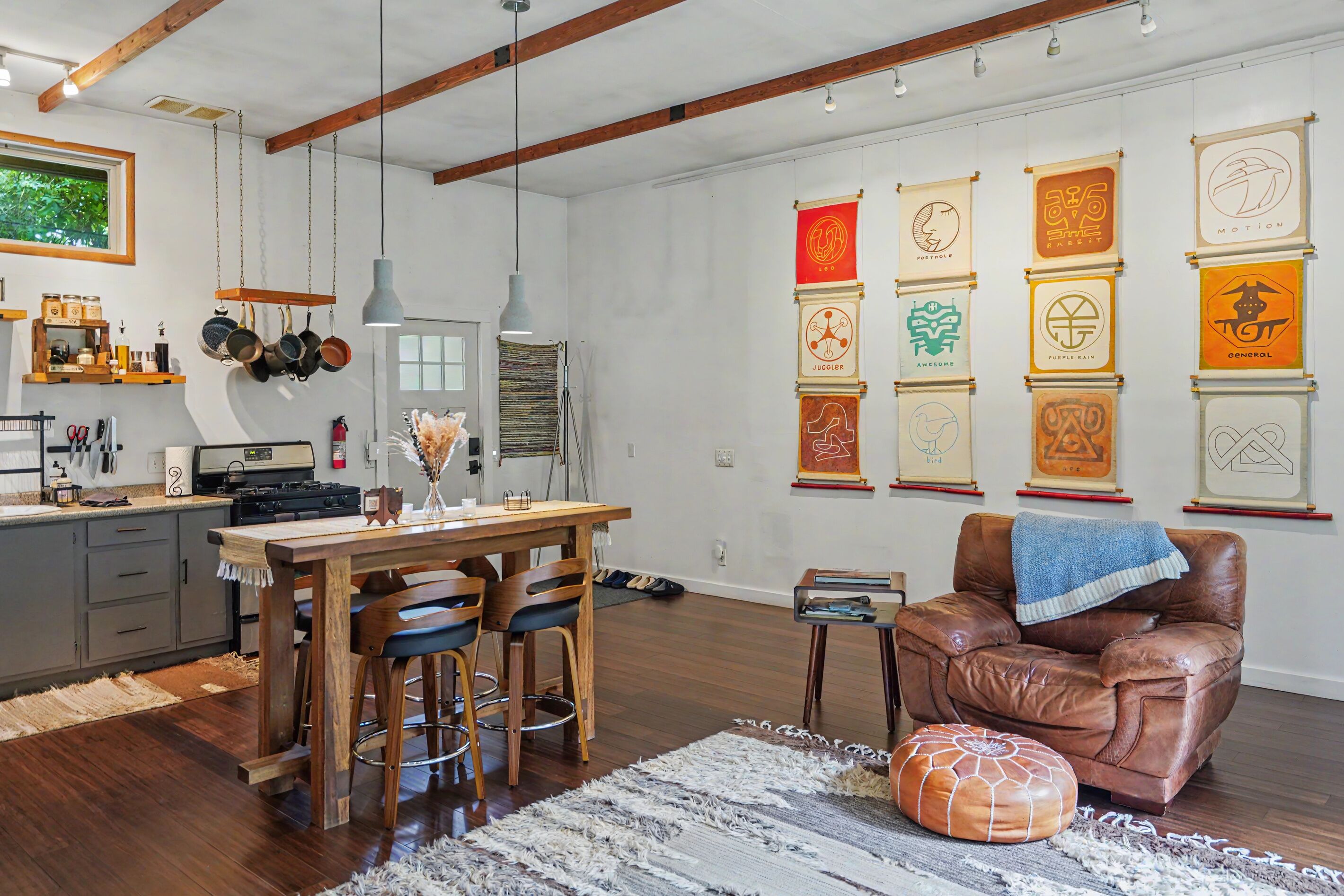 A modern kitchen with wooden cabinets, a dining table with chairs, and a hanging pot rack.