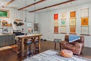 A modern kitchen with wooden cabinets, a dining table with chairs, and a hanging pot rack. - Art Studio Retreat with Sauna Fireplace Forest Views | Dream House in the Gunks (Kerhonkson)