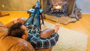 Eine Person liegt auf einem braunen Ledersofa in einem Raum mit einem Steinkamin und hält ein Glas.