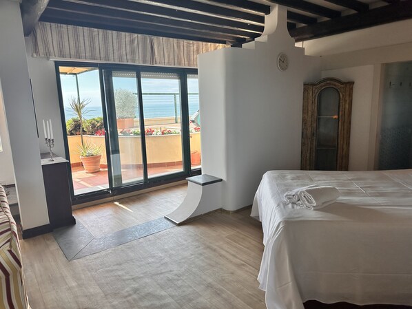 Un dormitorio con una cama grande, vistas al exterior a través de una puerta corrediza de vidrio, techo de madera y una mesita de noche pequeña.