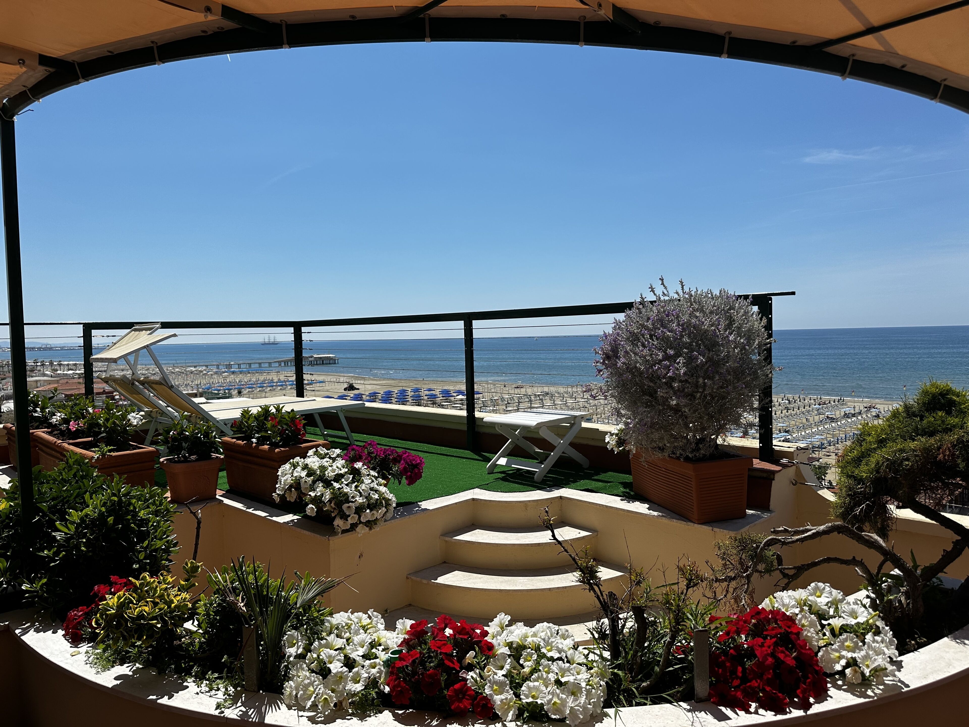 Un balcón con vista a la playa, plantas en macetas y un espacio para sentarse.