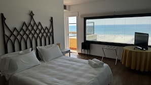 A bedroom with a large bed, a television on a small table, and a view of the beach through a window. - Penthouse Piccadilly with Jacuzzi (Lido di Camaiore)