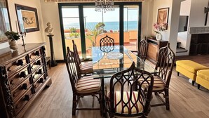 A dining area with a glass table surrounded by chairs, a wooden cabinet, and a view of the sea through large windows. - Penthouse Piccadilly with Jacuzzi (Lido di Camaiore)