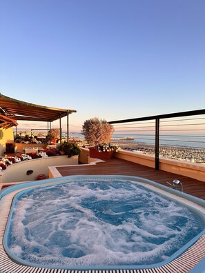 Ein Whirlpool auf einer Holzterrasse mit Blick auf das Meer und ein Gebäude mit Außenplätzen.