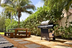 An outdoor patio with a grill, a wooden table, and a bench.