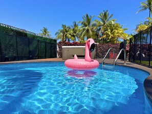 A swimming pool with clear blue water, a pink flamingo float, and palm trees in the background.