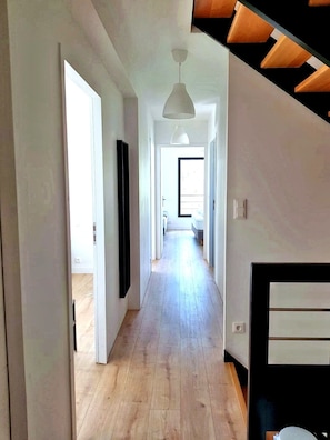 A long, narrow hallway with wooden flooring, white walls, and a white pendant light. There is a door on the left and a staircase on the right. - TY BRAZ – Very large house, a 3-minute walk from the beach (on the Baie de Quiberon side) (Saint-Pierre-Quiberon)