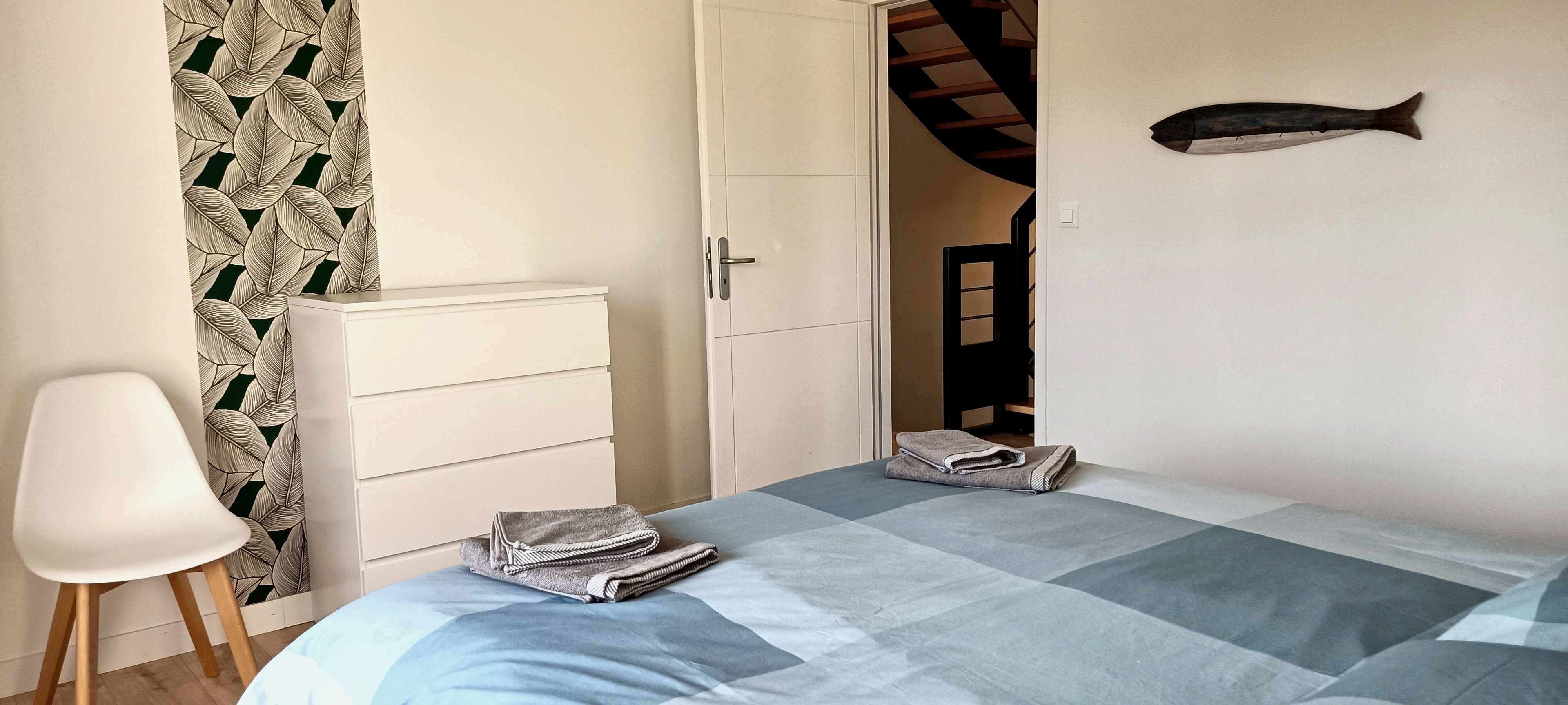 Une chambre à coucher comprenant un lit, une chaise, une commode, un élément de décoration représentant un poisson et un escalier.