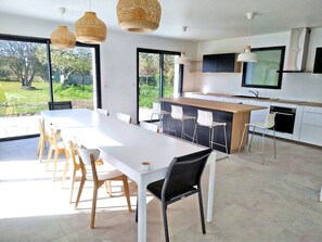 Une cuisine moderne dotée d’un îlot central, de meubles blancs et d’un grand espace de salle à manger avec des chaises.