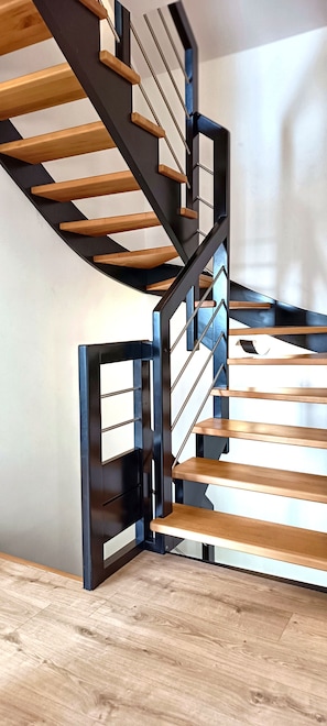 Un escalier moderne en colimaçon, avec des marches en bois et des rampes en métal noir.
