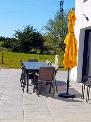 Eine Terrasse im Freien mit Tisch und Stühlen, einem gelben Sonnenschirm und Blick auf eine grüne Landschaft.