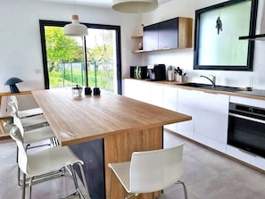 Une cuisine moderne avec un îlot central en bois, des chaises blanches, un plan de travail noir et une grande fenêtre.