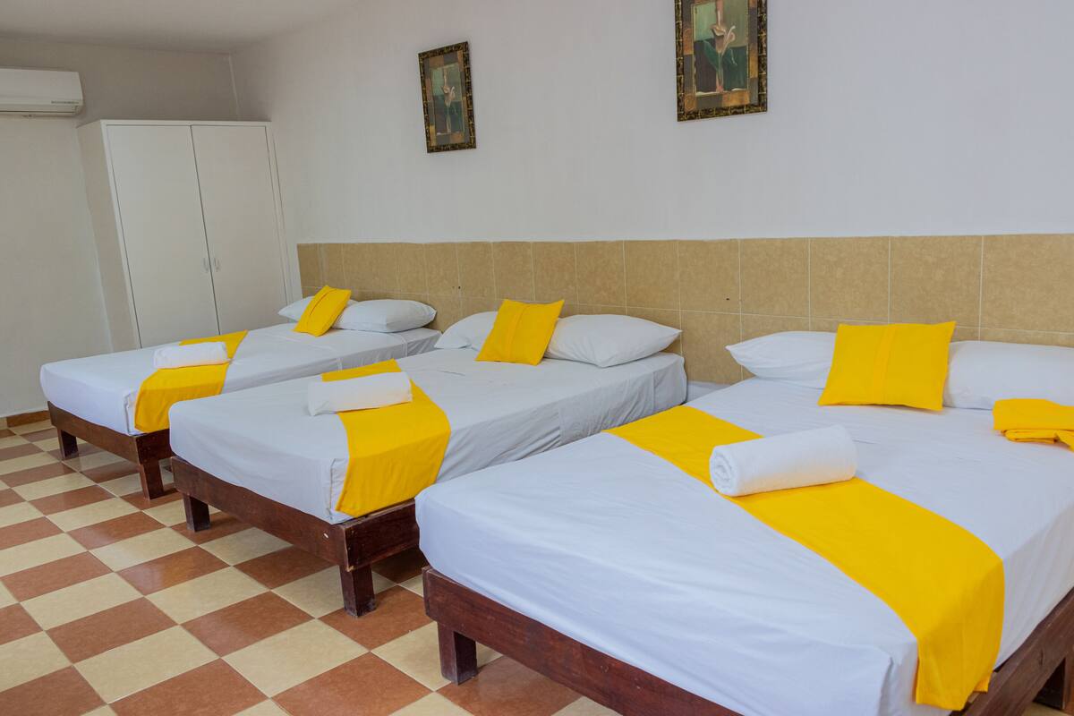 A hotel room with four single beds, each with a white mattress and yellow accents, arranged in a row.