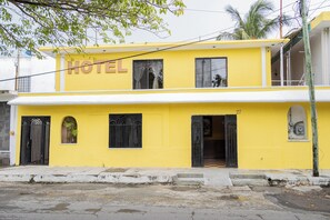 A two-story yellow building with a sign that reads "HOTEL" above the entrance. There are black metal gates and windows, and a small balcony on the upper floor.