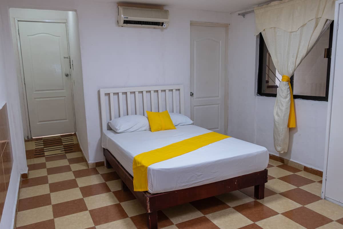 A room with a bed, a window with curtains, a radiator, and a door.