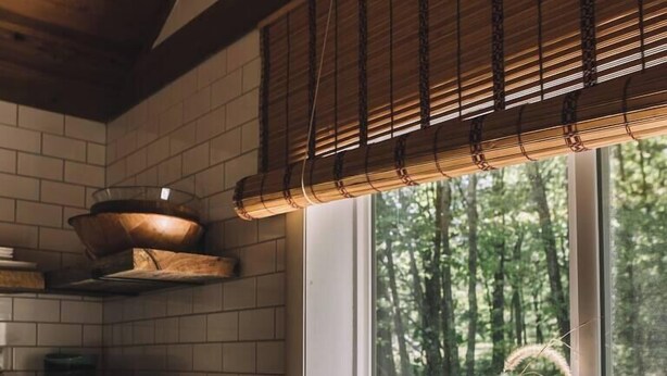 A kitchen with wooden shelves, a window with a view of trees, and a vase with flowers on the windowsill.