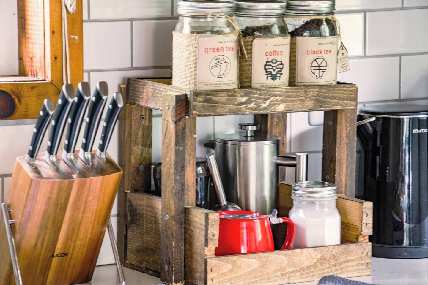 A kitchen counter with a wooden crate holding jars labeled 'green tea,' 'coffee,' and 'black tea.'