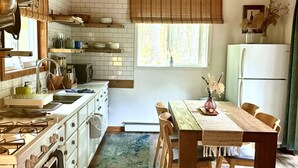 A kitchen with wooden ceiling, white cabinets, a dining table with chairs, and a refrigerator.