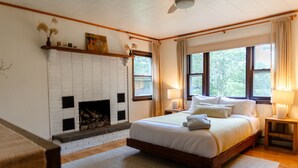 A bedroom with a large bed, a fireplace, and two windows with curtains.