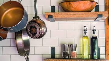 A kitchen with hanging pots, a wooden bowl on a shelf, and bottles of oil and spices.
