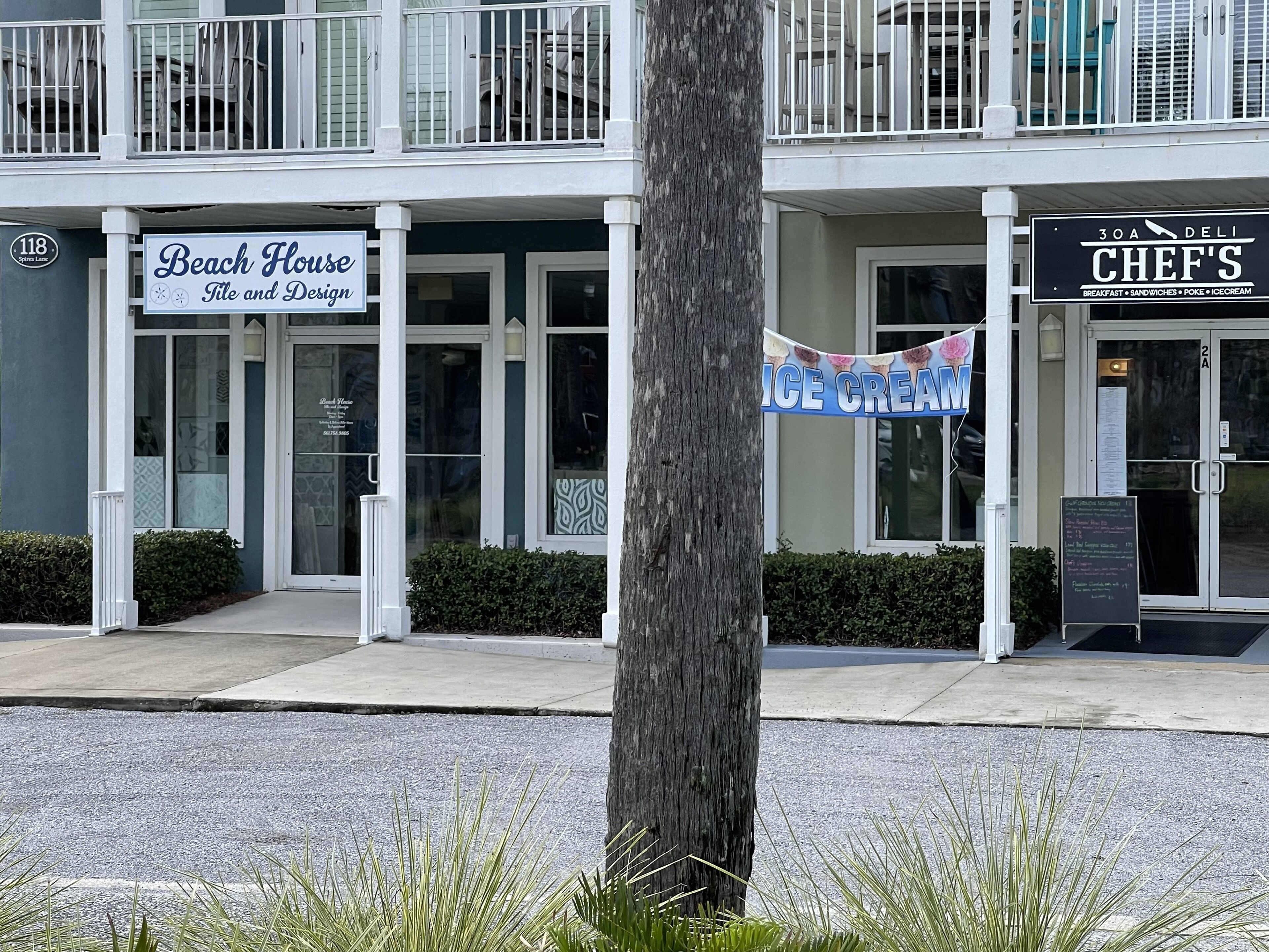Ein Gebäude mit Schildern für 'Beach House Tile and Design' und 'Chef's Deli', sowie einem Banner mit der Aufschrift 'Ice Cream'.