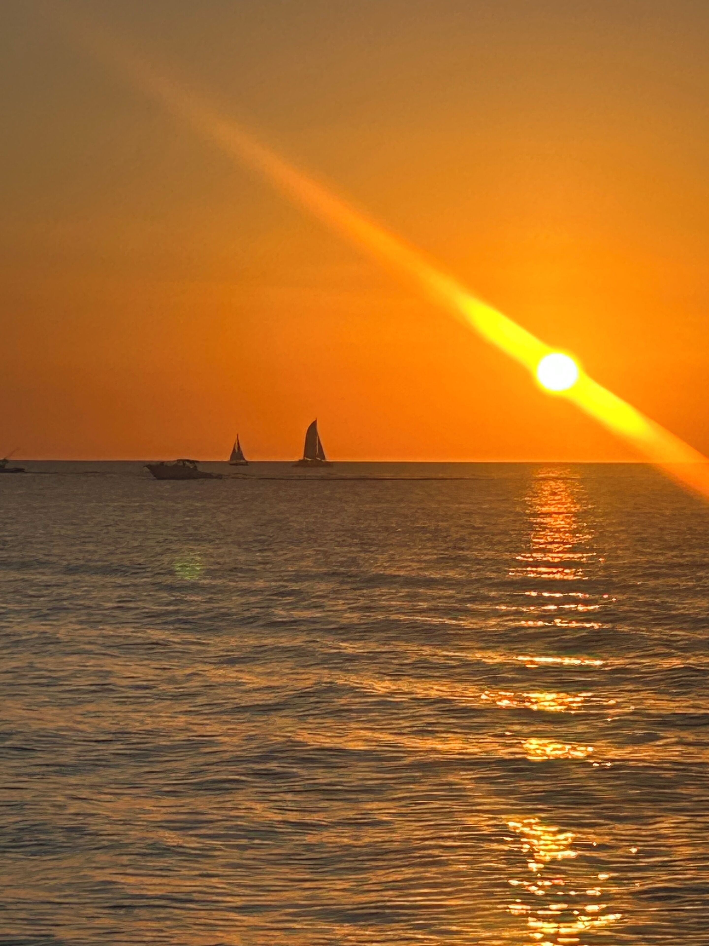 Un sol ponent sobre un mar tranquil amb dos velers.