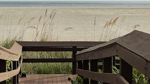 Eine Holzterrasse mit Blick auf einen Strand, hohe Gräser und den Ozean im Hintergrund.