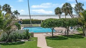 A pool area with a clear view of the ocean, surrounded by palm trees and a well-maintained lawn. - Marco Island  Beach absolutely breathtaking view of Sunset from  the balcony   (Marco Island)