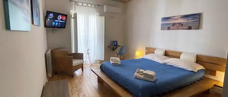A bedroom with a wooden bed, a desk with a chair, a TV, and a window with curtains.