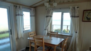 Zona pranzo con tavolo e sedie in legno, vista sul mare attraverso ampie finestre e una porta che dà all'esterno.