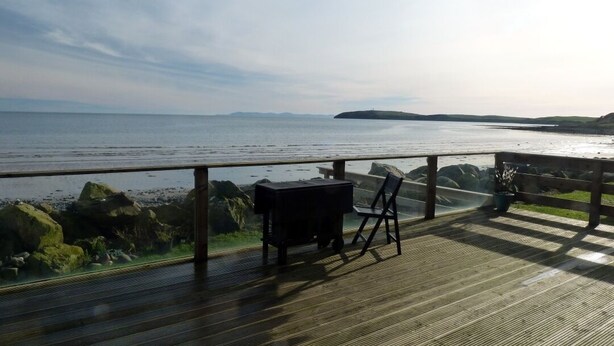 Un terrazza in legno con una griglia e sedie che si affaccia su un corso d'acqua.
