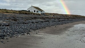 Una casa su una spiaggia rocciosa con un arcobaleno nel cielo.