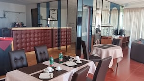 A dining area with a table set for two, a bar area, and a seating area with a sofa. - Miga Hotel Airport (Isola di Capo Rizzuto)