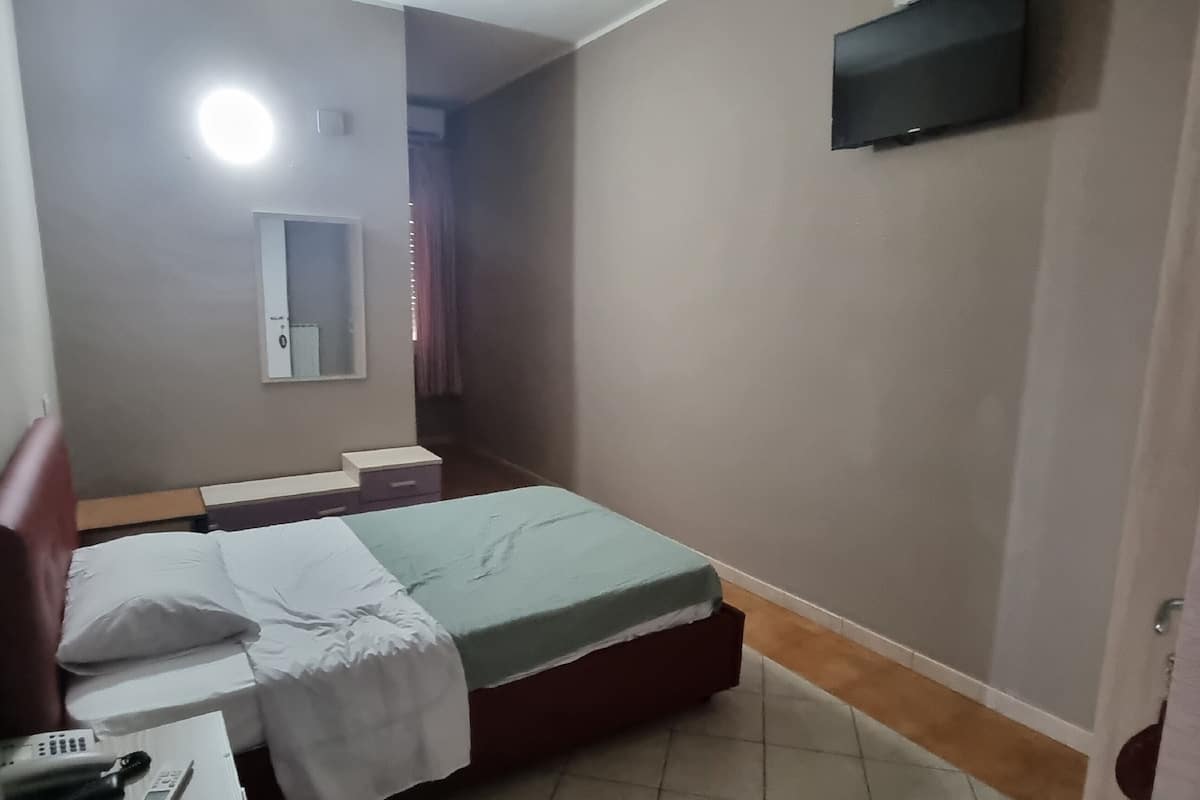 A small, neatly arranged bedroom with a bed, bedside table, and a mounted TV.