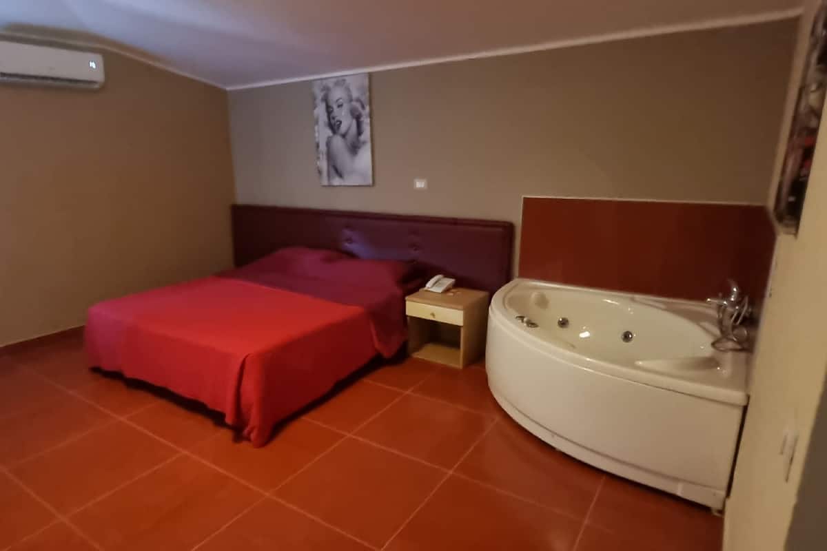 A small hotel room with a bed, a nightstand, a telephone, and a bathtub.