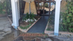 A hotel entrance with a covered walkway, stone walls, and potted plants. - Miga Hotel Airport (Isola di Capo Rizzuto)