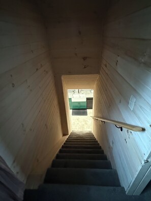 A wooden staircase leading to a room with a green door and a white wall.