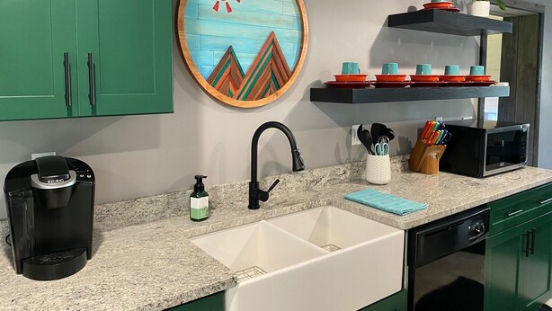 A kitchen with green cabinets, a coffee maker, a sink, a microwave, and a shelf with dishes. - Colorful Cape Cod (Lexington)