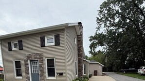 A two-story residential building with a front entrance, a small porch, and a driveway leading to a parked vehicle. - Colorful Cape Cod (Lexington)